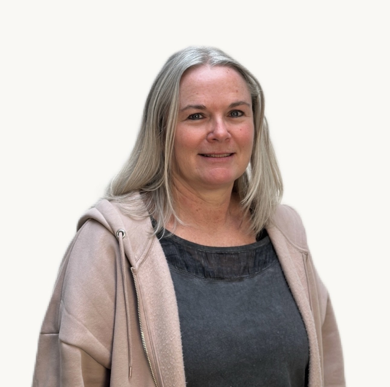 Porträt einer lächelnden Frau mit blondem Haar im beigefarbenen Hoodie vor hellem Hintergrund