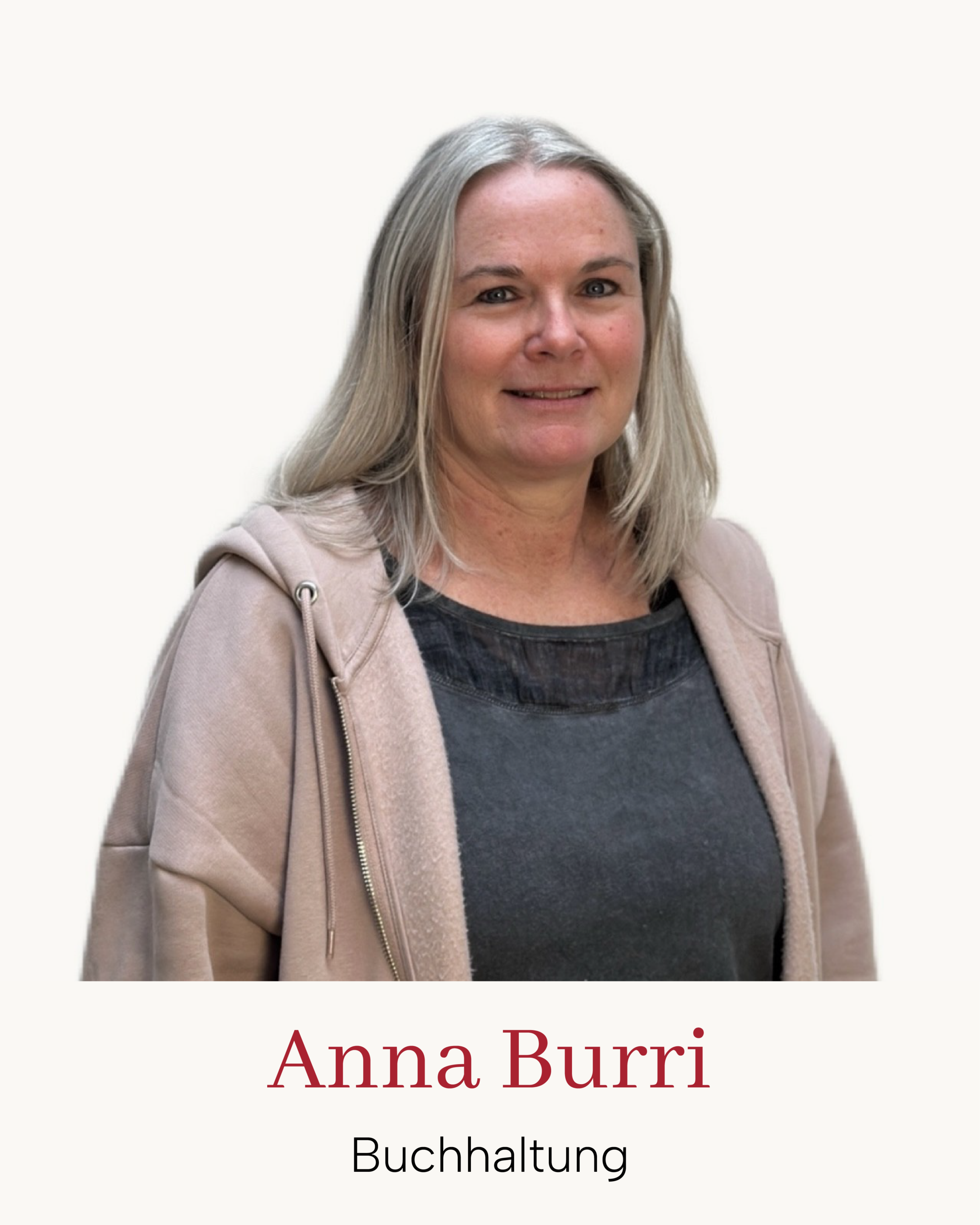 Porträt: Mitarbeiterin im Buchhaltungsteam, lächelnd, beigefarbener Hoodie, dunkles Top, neutraler Hintergrund.